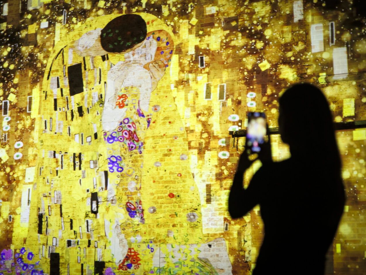 Jugendliche filmt mit dem Handy eine Lichtinstallation mit dem Bild "Der Kuss" von Gustav Klimt